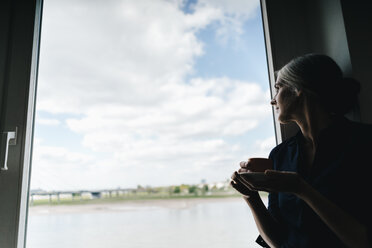 Geschäftsfrau schaut aus dem Fenster in einem Büro am Wasser - KNSF01813