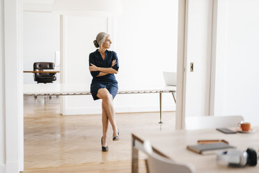 Businesswoman sitting on table in modern office - KNSF01820