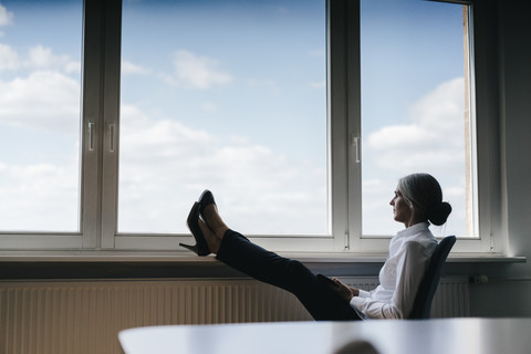 Geschäftsfrau im Büro sitzt am Fenster und schaut hinaus, lizenzfreies Stockfoto