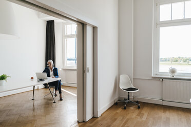 Businesswoman working on laptop in office - KNSF01827