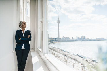 Businesswoman looking out of window in waterfront office - KNSF01828