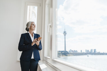 Businesswoman looking out of window in waterfront office - KNSF01830