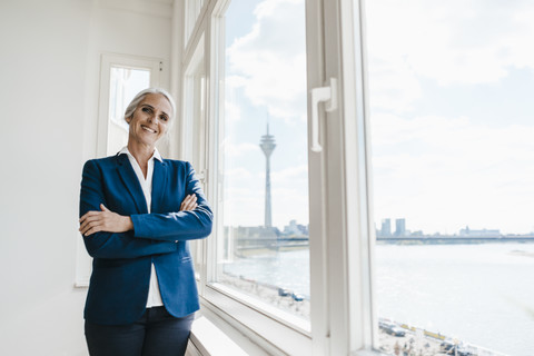 Porträt einer selbstbewussten Geschäftsfrau am Fenster eines Büros am Wasser, lizenzfreies Stockfoto