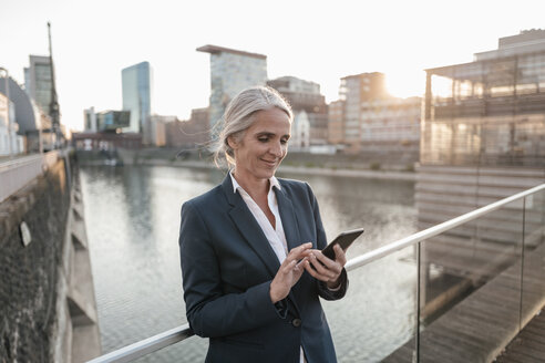 Smiling businesswoman using cell phone on bridge - KNSF01856