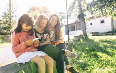 Drei Mädchen benutzen ihre Smartphones im Freien - MGOF03435