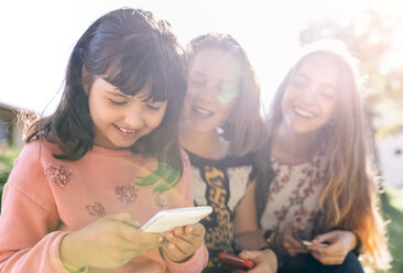 Three happy girls using their smartphones outdoors - MGOF03437