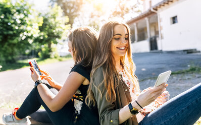 Zwei glückliche Mädchen benutzen ihre Smartphones im Freien - MGOF03441