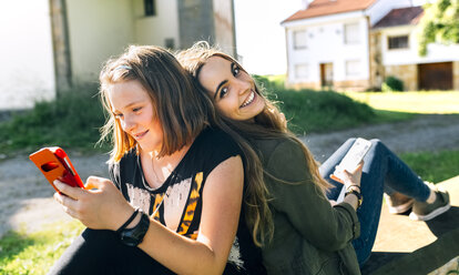 Zwei glückliche Mädchen benutzen ihre Smartphones im Freien - MGOF03442