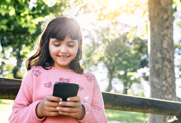 Smiling girl sending messages with her smartphone - MGOF03451