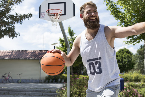 Lachender Mann spielt Basketball auf einem Platz im Freien, lizenzfreies Stockfoto