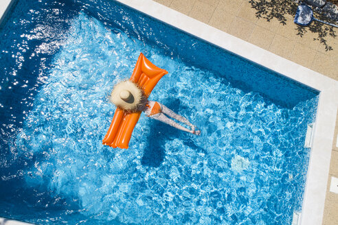 Rückenansicht einer Frau, die sich auf einer orangefarbenen Luftmatratze im Schwimmbad entspannt - MAEF12347