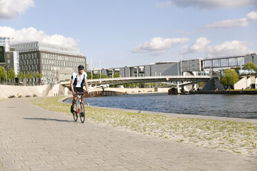 Junger Mann fährt Fahrrad am Wasser in der Stadt - FKF02428