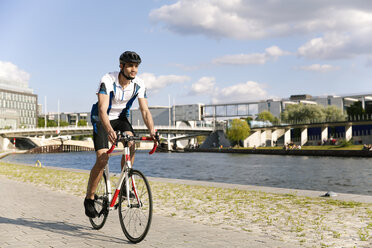 Junger Mann fährt Fahrrad am Wasser in der Stadt - FKF02429