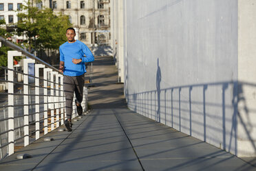 Young man running on footbridge in the city - FKF02431