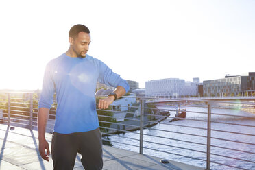 Athlete on bridge in the city checking his smartwatch - FKF02437