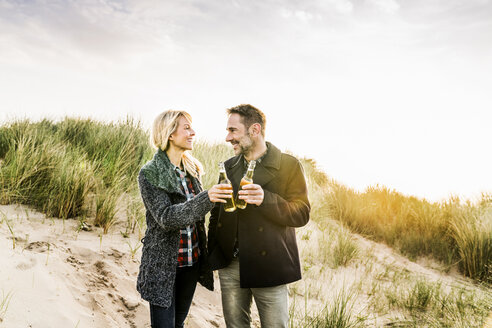 Happy couple in dunes clinking beer bottles - FMKF04202