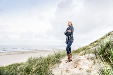 Smiling woman standing in dunes - FMKF04212