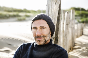 Portrait of smiling man at fence on the beach - FMKF04213