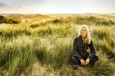 Portrait of smiling woman sitting in dunes stock photo
