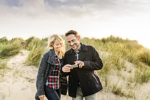 Happy couple in dunes sharing cell phone stock photo