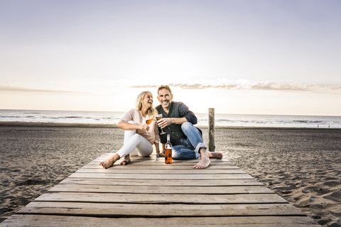 Glückliches Paar mit Weingläsern auf der Promenade am Strand bei Sonnenuntergang, lizenzfreies Stockfoto