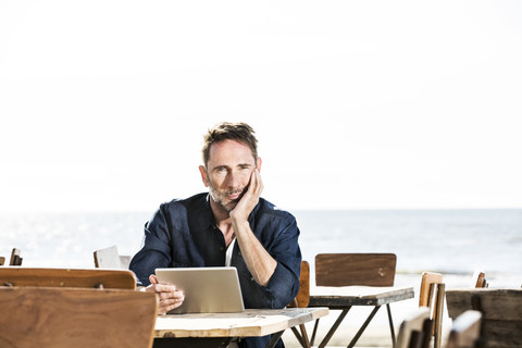 Mann mit Tablet in einem Cafe am Strand sitzend, lizenzfreies Stockfoto
