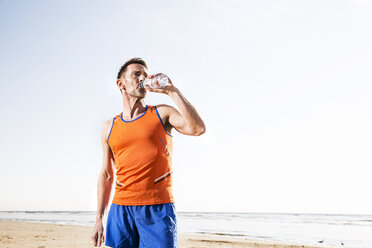 Athlete drinking from bottle on the beach - FMKF04246