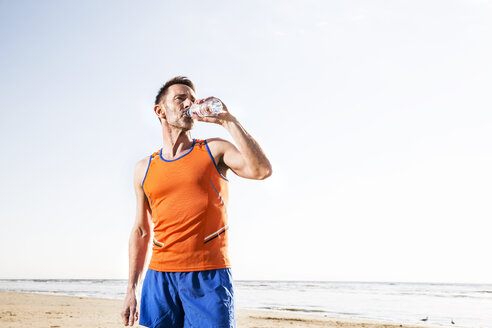 Sportler trinkt am Strand aus einer Flasche - FMKF04246