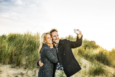 Happy couple in dunes taking a selfie - FMKF04247