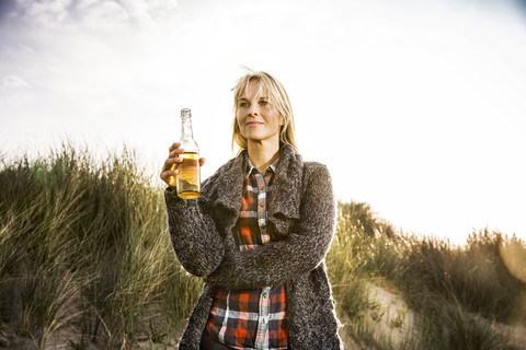 Lächelnde Frau trinkt ein Bier in den Dünen, lizenzfreies Stockfoto