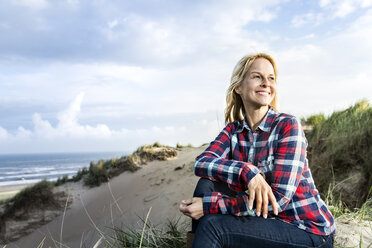 Smiling woman sitting in dunes - FMKF04256