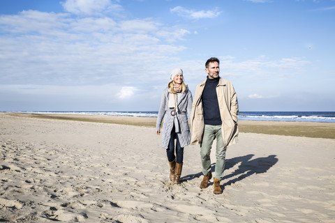 Paar in warmer Kleidung beim Spaziergang am Strand, lizenzfreies Stockfoto