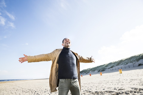 Glücklicher Mann mit ausgestreckten Armen am Strand stehend, lizenzfreies Stockfoto