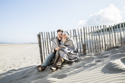 Lächelndes Paar in Decke eingewickelt am Strand, lizenzfreies Stockfoto
