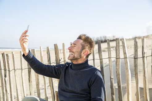 Mann macht ein Selfie am Zaun am Strand - FMKF04280