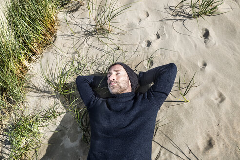 Mann mit Wollmütze in einer Stranddüne liegend - FMKF04284