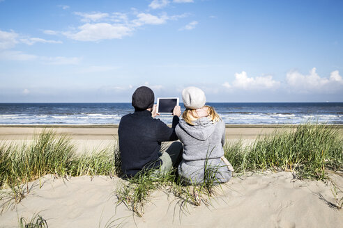 Paar sitzt in den Dünen am Strand mit Tablet - FMKF04285