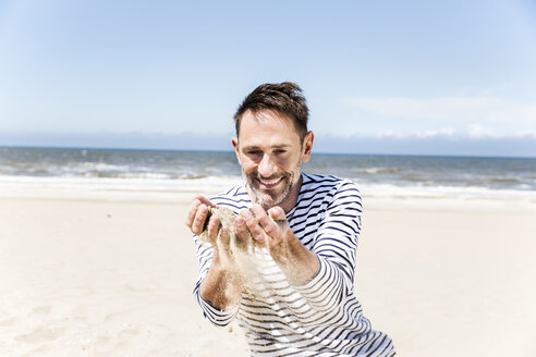 Glücklicher Mann am Strand, der Sand durch seine Hände rieseln lässt - FMKF04289