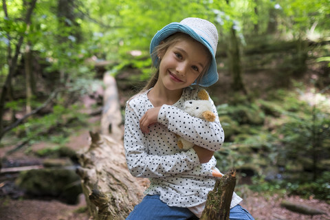 Porträt eines lächelnden kleinen Mädchens mit Kuscheltier im Wald, lizenzfreies Stockfoto