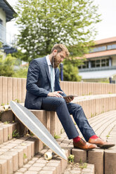 Geschäftsmann mit Skateboard, der ein Tablet und Kopfhörer benutzt - MAEF12360