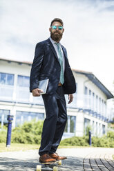 Portrait of businessman with sunglasses and tablet standing on skateboard - MAEF12364