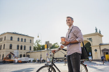 Lächelnder Mann mit Fahrrad und Kaffee zum Mitnehmen in der Stadt - DIGF02559