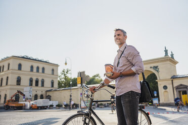 Smiling man with bicycle and takeaway coffee in the city - DIGF02559