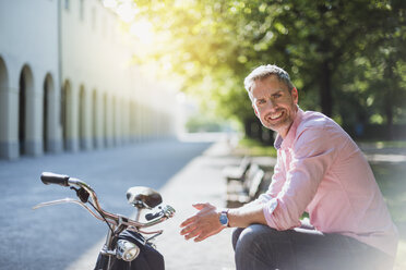 Porträt eines lächelnden Mannes mit Fahrrad, der auf einer Parkbank sitzt - DIGF02569