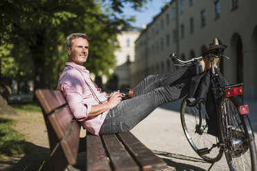 Mann mit Fahrrad und altmodischer Kamera entspannt sich auf einer Parkbank - DIGF02574