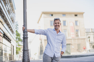 Portrait of happy man at lamp pole in the city - DIGF02583