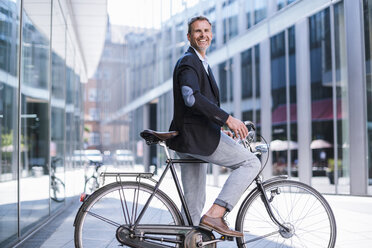 Smiling businessman on bicycle in the city - DIGF02596