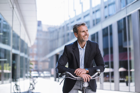 Smiling businessman on bicycle in the city stock photo