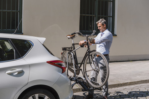 Mann befestigt Fahrrad auf Anhänger am Auto, lizenzfreies Stockfoto