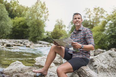 Hiker sitting at riverbank with map - DIGF02606